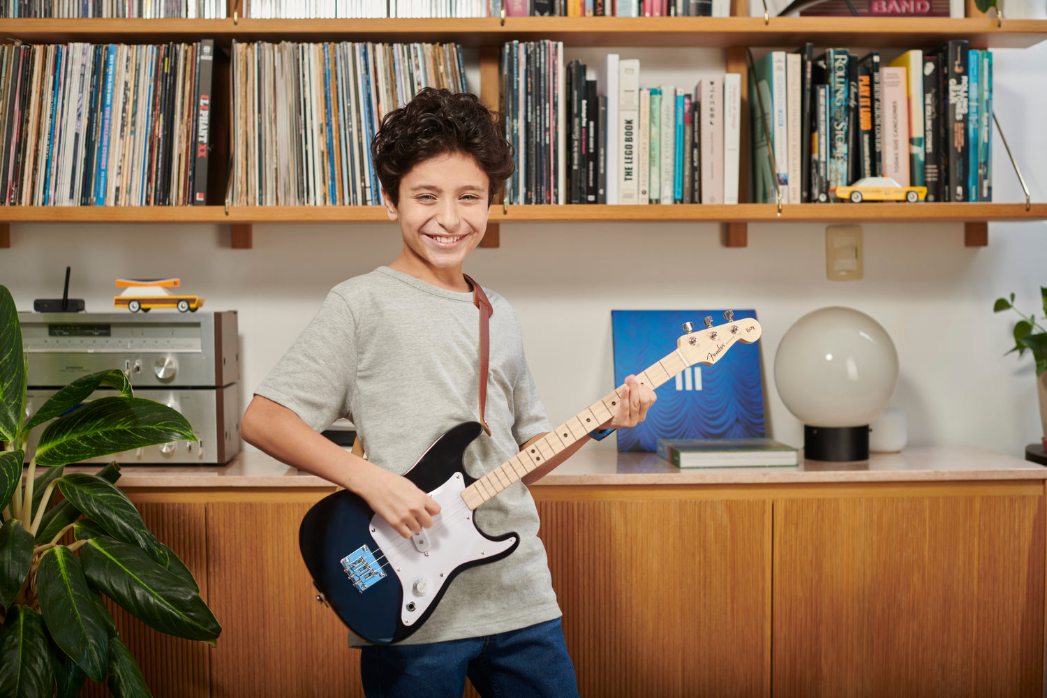 a boy holding a guitar in front of a bookshelf